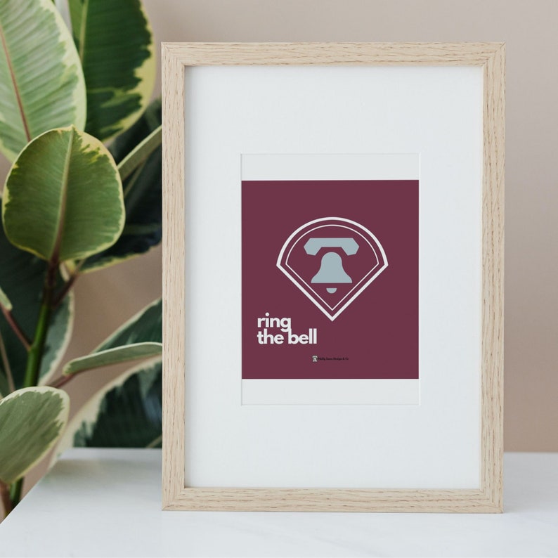 May include: A framed print with a maroon background and a white baseball diamond with a bell inside. The text "ring the bell" is below the diamond.