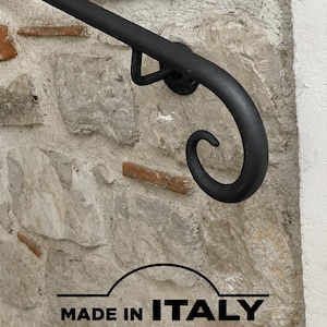 May include: A matte black metal handrail featuring a curved, scroll-shaped end detail. The handrail is mounted to a textured stone wall. Below the handrail, a graphic includes the text MADE IN ITALY and FERMEG with a tricolor line.