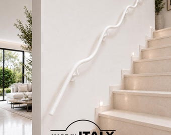 May include: A white, wavy-shaped metal handrail mounted to a wall alongside a staircase. The handrail features a continuous, flowing design with multiple support brackets. Below the staircase, a logo reads MADE IN ITALY FERMEG.