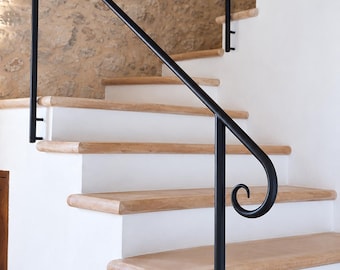 May include: A staircase featuring white risers and light brown stone treads, complemented by a black metal handrail with a decorative scroll end. The stairs are positioned against a textured, light brown stone wall, creating a contrast between the smooth white surfaces and the natural stone elements.