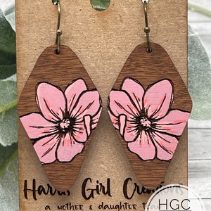 Könnte beinhalten: Holzohrringe in Diamantform mit einem rosa Blumendesign. Die Ohrringe haben einen dunkelbraunen Holzmaserungshintergrund und goldfarbene Haken. Auf der Präsentationskarte ist der Text "Harris Girl Crafts" und "HGC DIGITAL DESIGNS" zu sehen.