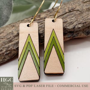 Puede incluir: Un par de pendientes de madera con un diseño geométrico. Los pendientes son rectangulares y presentan un patrón de chevron verde sobre un fondo marrón claro.