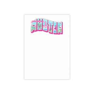 May include: A vintage-style postcard design featuring the word "Austin" in pink and blue lettering with a cityscape illustration inside the letters. The text "Greetings from" is above the word "Austin".