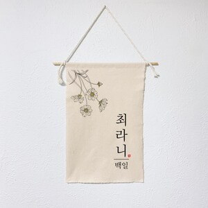 May include: A beige canvas wall tapestry with a black and white illustration of a bouquet of flowers. The text "최라니" is written in black with the word "백일" in red below it.