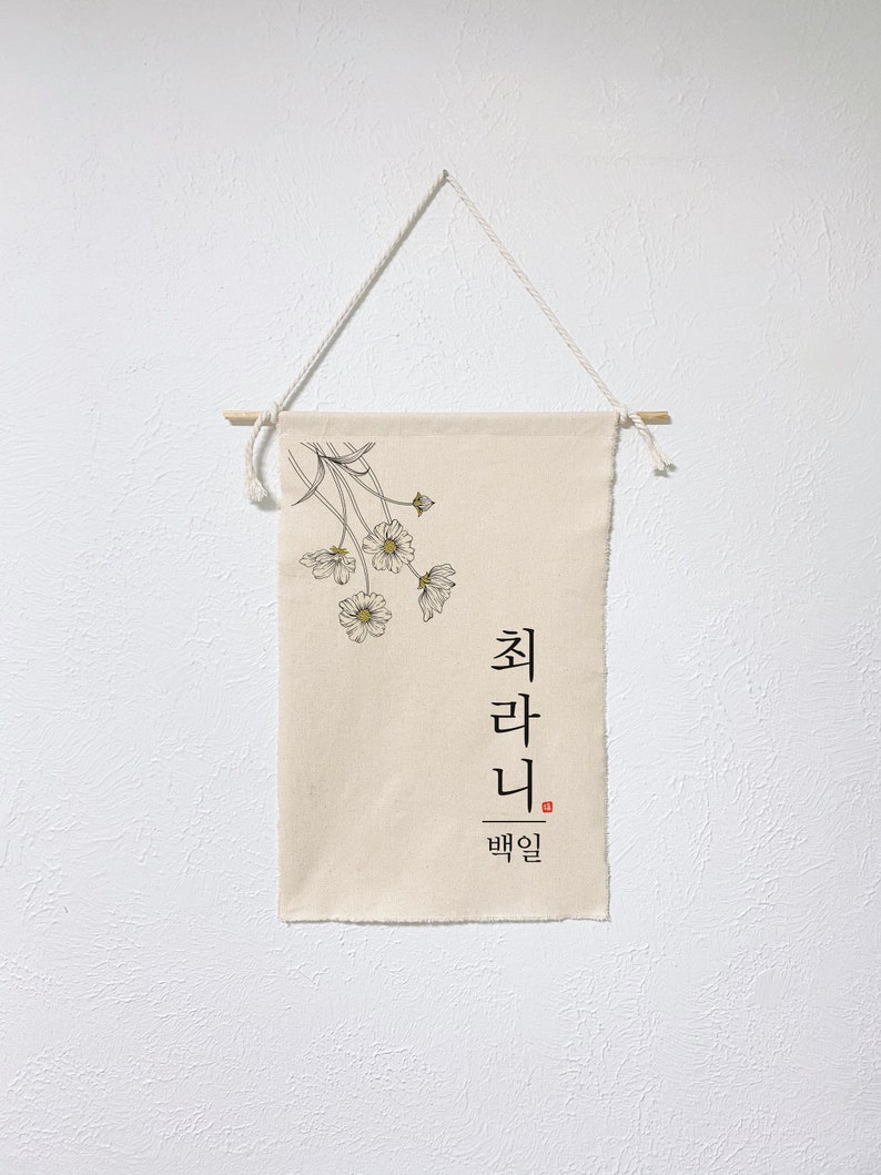 May include: A beige canvas wall tapestry with a black and white illustration of a bouquet of flowers. The text "최라니" is written in black with the word "백일" in red below it.