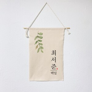 May include: A beige canvas wall hanging with a watercolor painting of green leaves and the Korean text "최선을 다할" which translates to "Do your best".