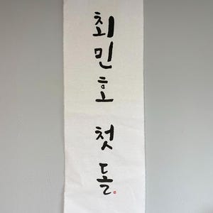 May include: White fabric banner with black calligraphy that reads "First Love" in Korean.