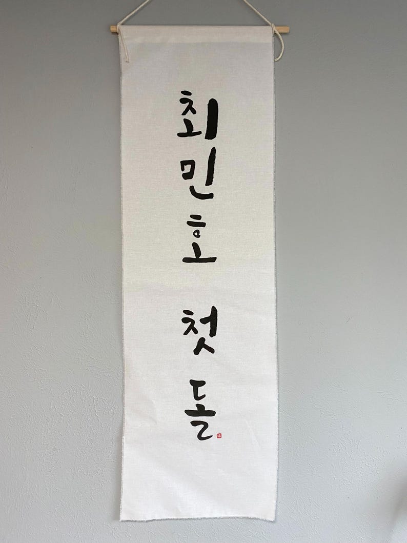 May include: White fabric banner with black calligraphy that reads "First Love" in Korean.