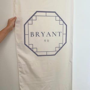 May include: A white fabric banner with a purple octagonal frame. The frame contains the text "BRYANT" and the Korean word "빛돌" in smaller font.