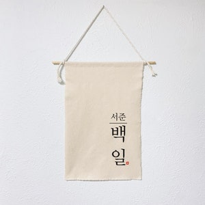 May include: A beige canvas banner with the Korean text "서른 밤" (meaning "Thirty Nights") in black calligraphy. The banner is hanging from a wooden dowel with string.