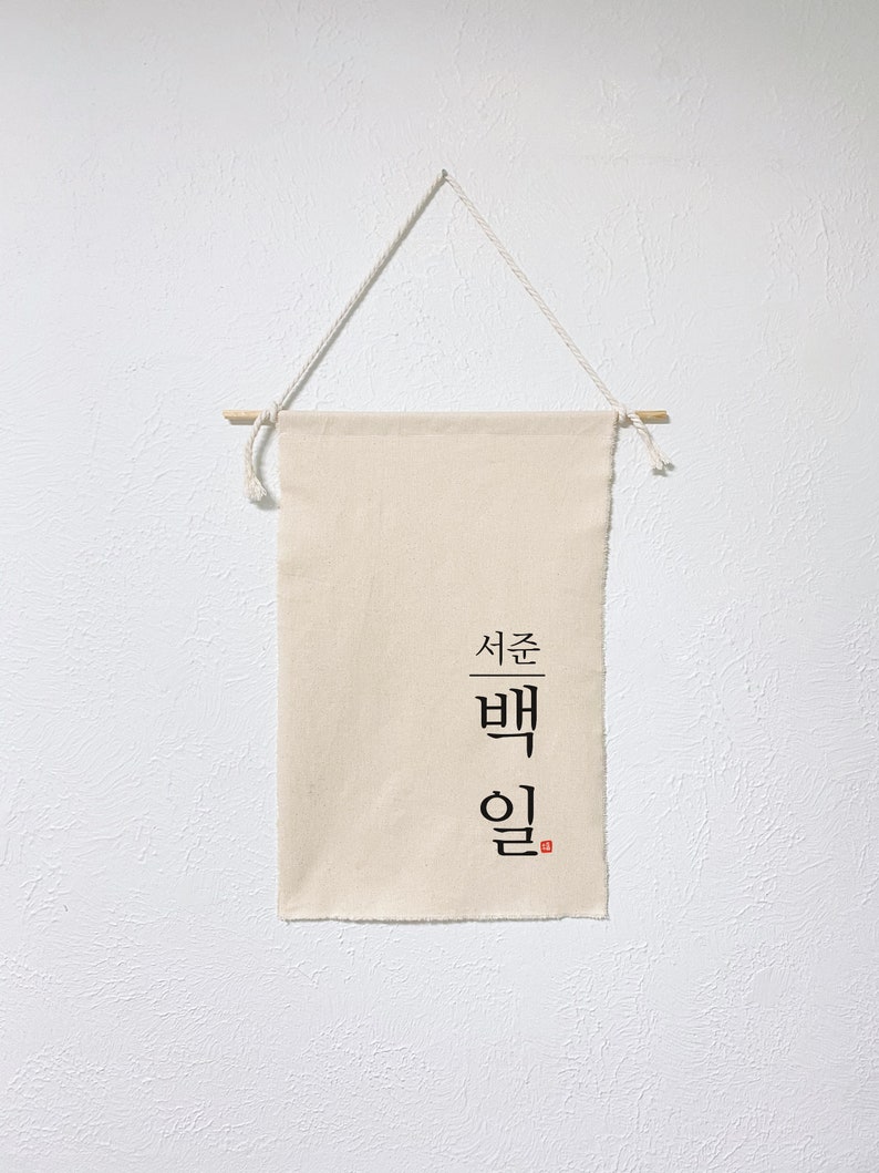 May include: A beige canvas banner with the Korean text "서른 밤" (meaning "Thirty Nights") in black calligraphy. The banner is hanging from a wooden dowel with string.
