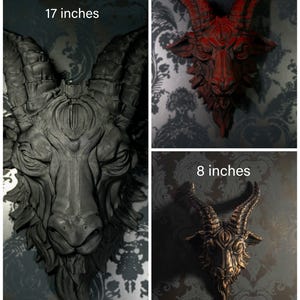 May include: Three goat head wall sculptures with horns and a third eye on the forehead. The largest is matte black and 17 inches, the medium is red and 12 inches, and the smallest is bronze-toned and 8 inches. Each piece features detailed fur.