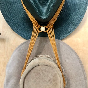 May include: Two hats connected by a brown cord. The top hat is dark blue and the bottom hat is light brown.