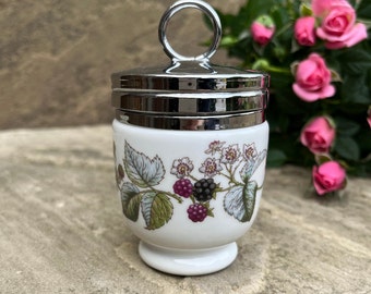 Könnte beinhalten: Ein weißer Eierbecher aus Keramik mit einem silbernen Deckel und einem Blumendesign mit Brombeeren und Blättern. Der Eierbecher hat einen kleinen Griff auf dem Deckel.