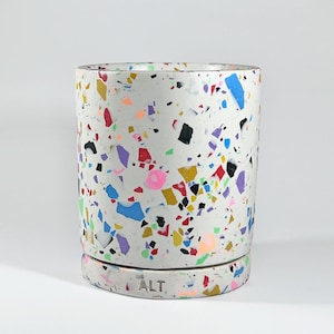 May include: White ceramic planter with a speckled pattern in various colours, including red, blue, yellow, green, and pink. The planter has a smooth, rounded base and the word "ALT" is printed on the bottom.
