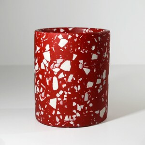 May include: Red terrazzo planter with white flecks. The planter is cylindrical and has a smooth, matte finish.