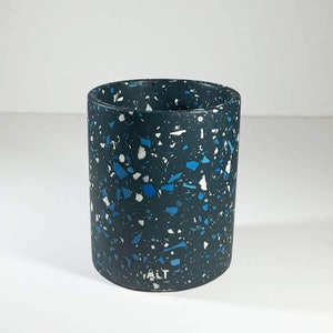 May include: A dark blue cylindrical container with a speckled pattern of white and blue flecks. The container has the word "ALT" printed on the bottom.