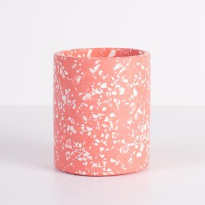 May include: A cylindrical container featuring a coral pink base with a scattered white terrazzo pattern. The exterior surface displays a smooth finish with irregular white flecks throughout. The word ALT is embossed in small letters near the base.