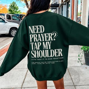 Może przedstawiać: Ciemnozielona bluza z długim rękawem z białym napisem na plecach: NEED PRAYER? TAP MY SHOULDER, LETS TAKE IT TO GOD TOGETHER, FOR WHERE TWO OR THREE GATHER IN MY NAME, THERE AM I WITH THEM oraz MATTHEW 18:20.