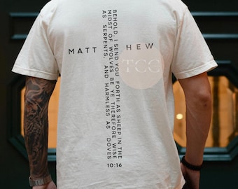 May include: Cream-coloured t-shirt with the text "MATT HEW TCC" and a quote from Matthew 10:16 printed vertically. The quote reads "BEHOLD, I SEND YOU FORTH AS SHEEP IN THE MIDST OF WOLVES BE YE THEREFORE WISE AS SERPENTS, AND HARMLESS AS DOVES 10:16."