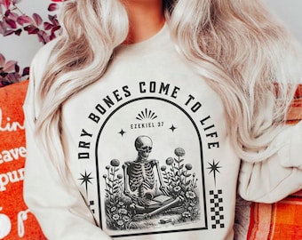 May include: Beige sweatshirt with a graphic of a skeleton meditating in a garden, surrounded by the text "DRY BONES COME TO LIFE" and "EZEKIEL 37". The sweatshirt is a crew neck style.