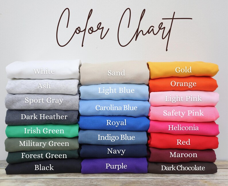 May include: A color chart displays folded fabric samples in various hues. The chart includes colors like white, ash, sport gray, dark heather, and black. Other colors include sand, light blue, royal, navy, and purple. The text "Color Chart" is written in cursive.