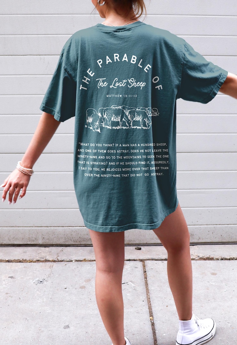 May include: Teal blue t-shirt with white text and a graphic of sheep. The text reads "The Parable of The Lost Sheep Matthew 18:11-13" and includes a passage from the Bible.