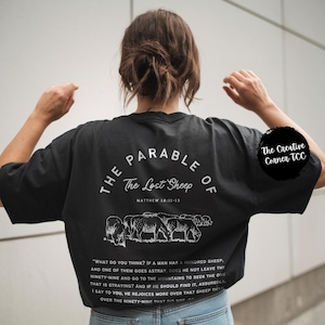 May include: Black t-shirt with white text that reads "The Parable of The Lost Sheep" and a scripture reference. The shirt also features a graphic of a flock of sheep.
