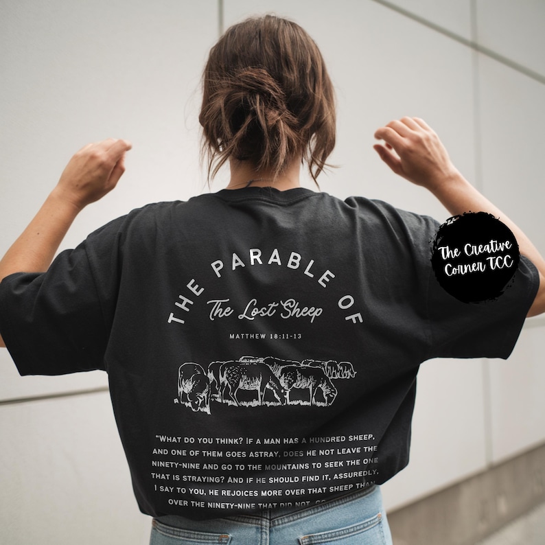 May include: Black t-shirt with white text that reads "The Parable of The Lost Sheep" and a scripture reference. The shirt also features a graphic of a flock of sheep.