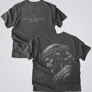 Puede incluir: Camiseta gris oscuro con el texto "THE WAY THE TRUTH THE LIFE" y una cruz. La parte trasera de la camiseta muestra una ilustraci&oacute;n detallada de una persona con una corona de espinas. La camiseta est&aacute; hecha de un material suave y c&oacute;modo.
