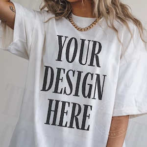 Może przedstawiać: Kremowa koszulka oversize z napisem "YOUR DESIGN HERE" pogrubioną czcionką. Koszulka ma krótkie rękawy i luźny krój. Widoczny jest złoty łańcuszek. Idealna do personalizacji i tworzenia własnych projektów.