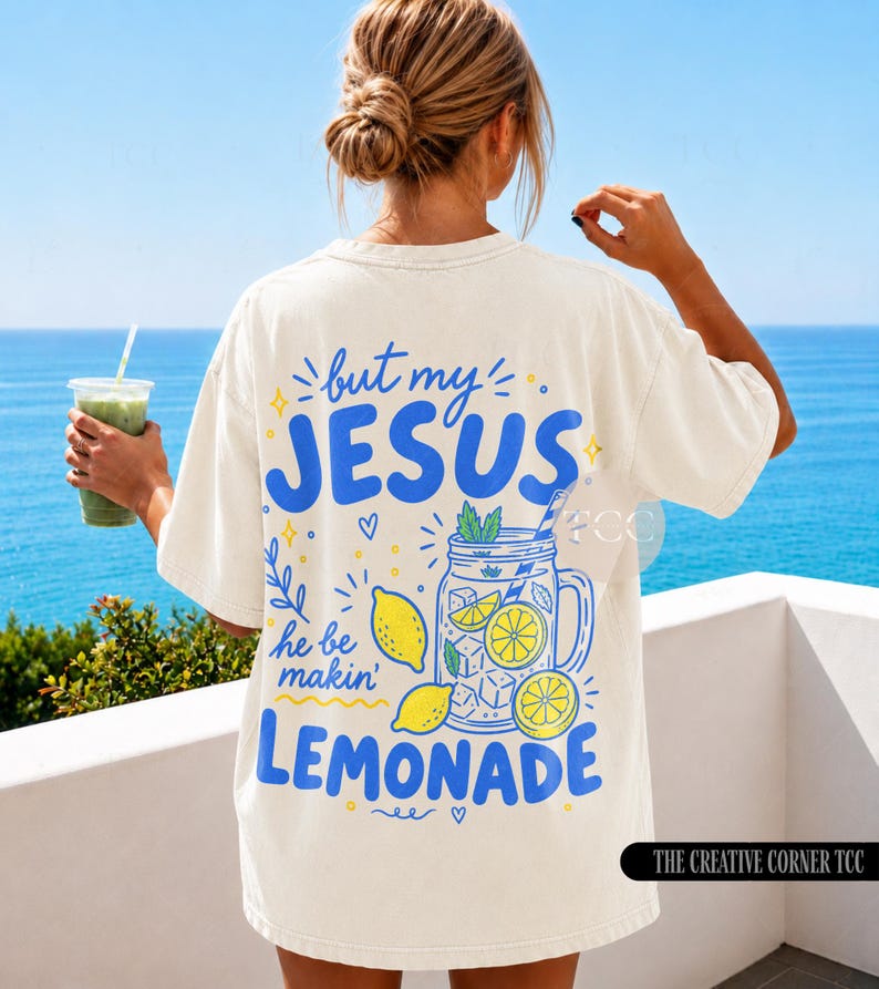 May include: An off-white short-sleeve t-shirt featuring a blue and yellow graphic on the back. The text reads, but my JESUS he be makin' LEMONADE, accompanied by illustrations of a mason jar filled with lemonade, ice cubes, and lemons.