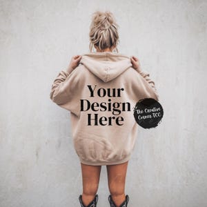 May include: A beige hoodie with the text "Your Design Here" printed on the back. The Creative Corner TCC is written in a circle on the right side of the hoodie.