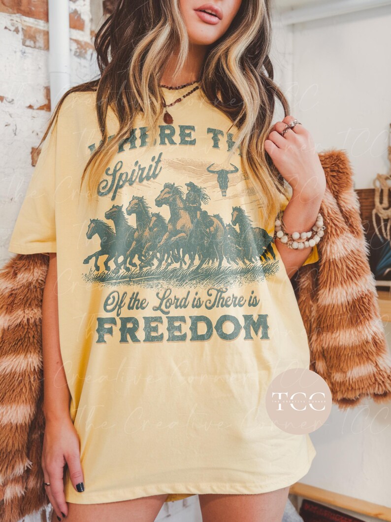 May include: Yellow graphic tee shirt with a vintage design featuring a herd of horses running across a field. The text on the shirt reads "Where the Spirit of the Lord is There is Freedom".