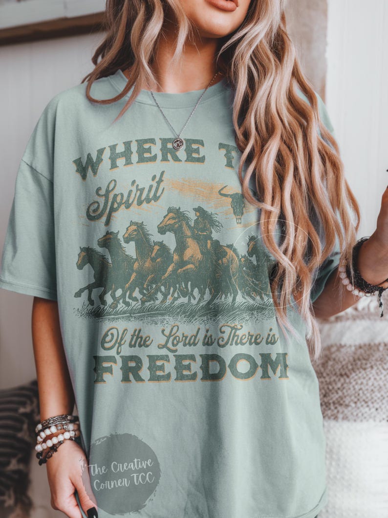 May include: A light blue t-shirt with a vintage graphic design featuring a group of horses running. The text on the shirt reads "Where the Spirit of the Lord is There is Freedom".
