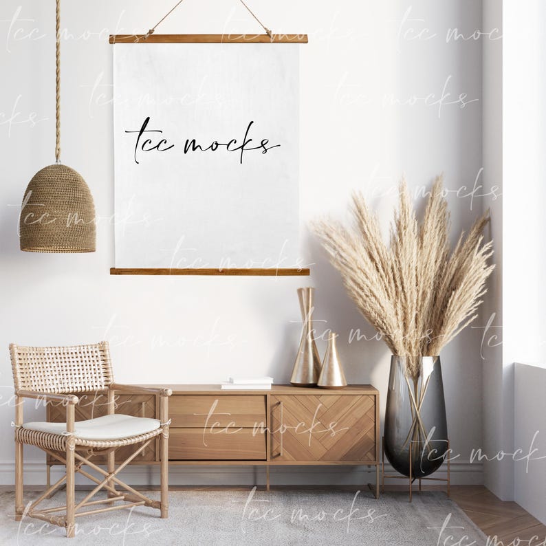 May include: A white canvas wall hanging with the text "tcc mocks" in black script. The hanging is displayed in a living room setting with a wooden dresser, a wicker chair, and a vase of dried pampas grass.
