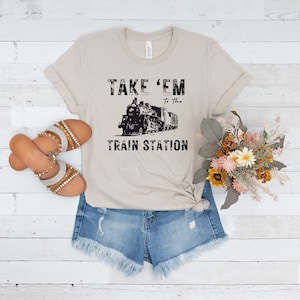 May include: A beige t-shirt with a black graphic of a train and the text "Take 'em to the train station".