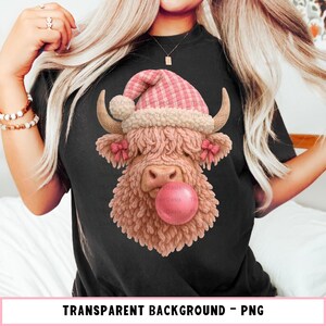 Puede incluir: Camiseta negra con una ilustración caprichosa de una vaca de las Tierras Altas con un gorro de Papá Noel rosa a cuadros y soplando una burbuja de chicle. La vaca tiene lazos rosas en las orejas. Texto "TRANSPARENT BACKGROUND - PNG" abajo.