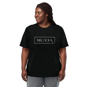 May include: A black t-shirt with a white box around the word "MUDDA" and a signature underneath.