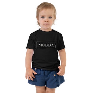 May include: A black toddler t-shirt with white text that reads "MUDDA" inside a white rectangle.