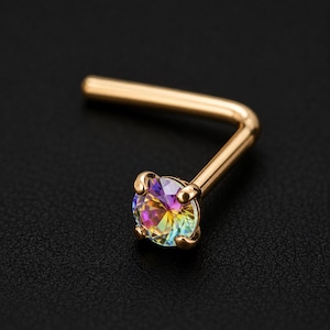Peut inclure: Un bijou de nez en forme de L avec une tige en métal doré poli et un cristal irisé rond serti de griffes. La pierre à facettes présente un spectre de couleurs arc-en-ciel, incluant du rose, du jaune, du bleu et du vert, reflétant la lumière.