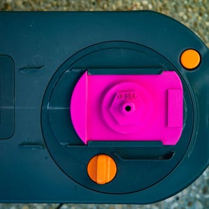 May include: A close-up of a dark gray plastic component with a bright pink central piece. The component has two orange circular buttons and the text "THETFORD" is visible. The design is geometric and functional.