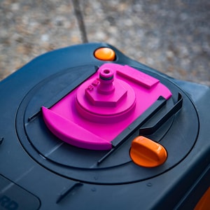 May include: Close-up of a dark blue RV water tank lid with a bright pink fill port and orange accents. The lid has a rounded shape with a textured surface and is designed for outdoor use.