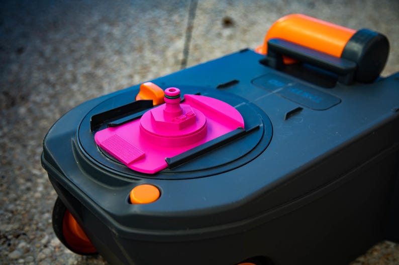 May include: A close-up of a black and gray portable toilet cassette with orange and pink accents. The cassette has a pink water inlet and an orange handle. The wheels are orange.
