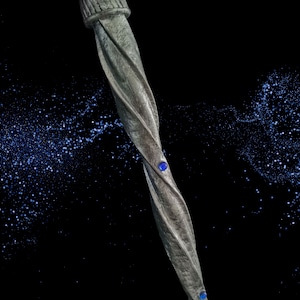 May include: A silver twisted metal wand with two blue gemstones. The wand is set against a black background with a scattering of blue glitter.