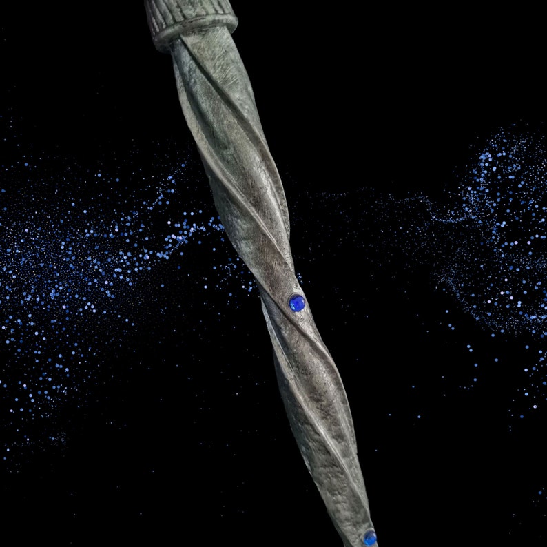 May include: A silver twisted metal wand with two blue gemstones. The wand is set against a black background with a scattering of blue glitter.