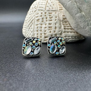 May include: A pair of silver square earrings with a cluster of iridescent blue and clear rhinestones.