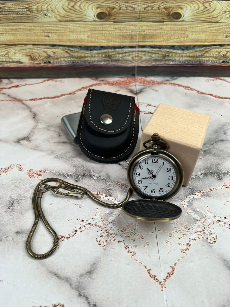 May include: A gold pocket watch with a white face and black Roman numeral hour markers. The watch is on a gold chain and has a black leather case with a gold button.