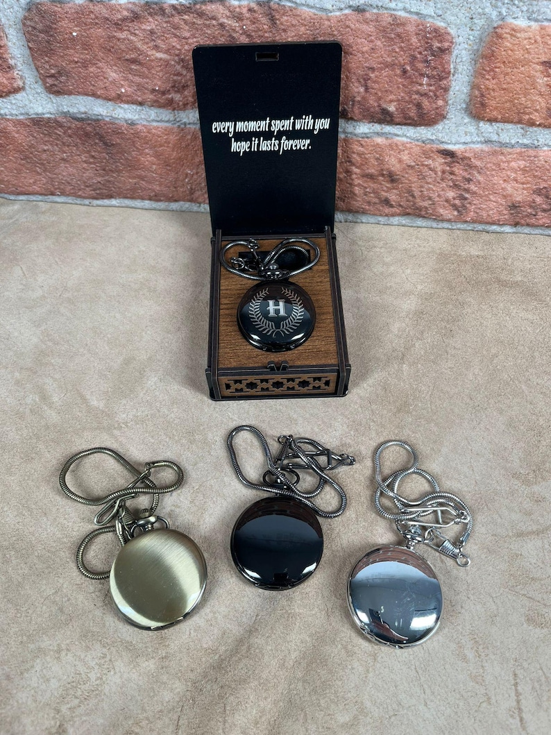 May include: A collection of pocket watches in various finishes: gold, black, and silver. One watch is displayed in a wooden box with the text "every moment spent with you hope it lasts forever." The watch in the box has an "H" initial.