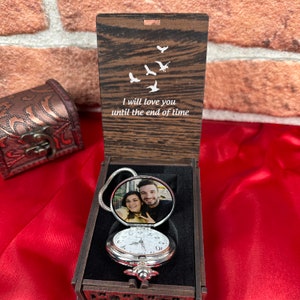 May include: A wooden box with a hinged lid, containing a silver pocket watch with a photo of a couple on the front. The lid of the box is engraved with the words "I will love you until the end of time" and a design of flying birds.